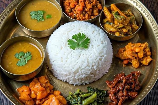 Authentic Nepali Dal Bhat thali set served on a brass plate with rice, lentil soup, curry, green spinach, and vegetable pickles.