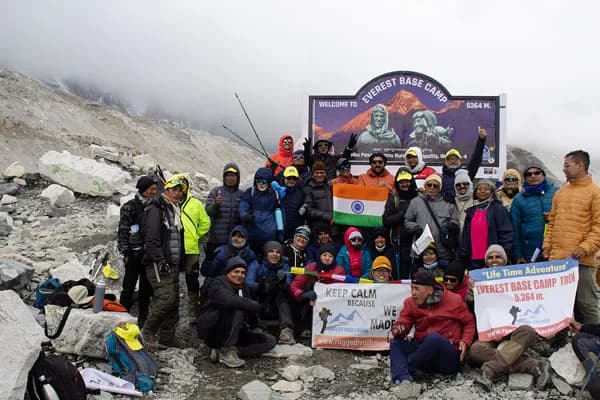 A large group of Indian trekkers gathered in front of the official Everest Base Camp sign board holding the national flag of India and banner.