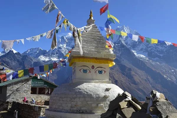 A white Buddhist stupa decorated with Buddha eyes and colorful prayer flags against the backdrop of snow-covered Mount Ama Dablam in the Everest region.