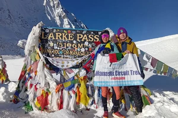 Trekkers posing proudly with a Manaslu Circuit Trek banner at the snowy Larkya La Pass sign at 5,106 meters