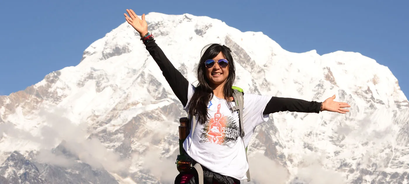 Happy female trekker standing with open arms against snow-capped Himalayan peak in Nepal