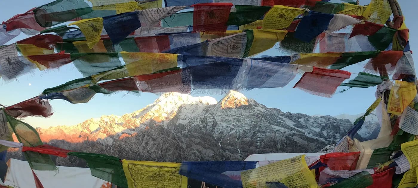 Buddhist prayer flags framing golden sunrise over snow-capped Himalayan mountain peaks during a trek near Pokhara.