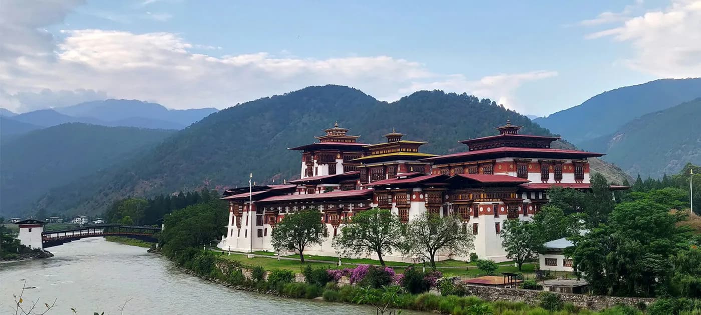 Panoramic view of Punakha Dzong fortress built at the confluence of two rivers in Bhutan with mountain backdrop.