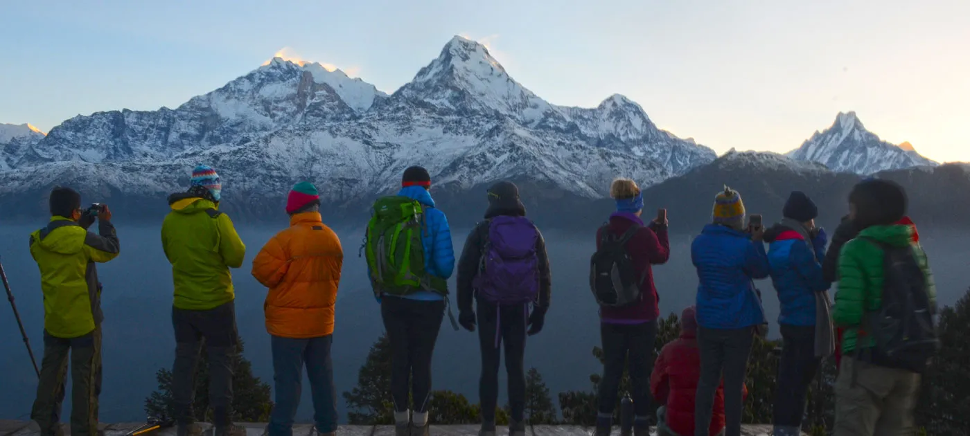 A large group of trekkers standing on a hill watching the golden morning light illuminate the snow-capped Himalayan peaks