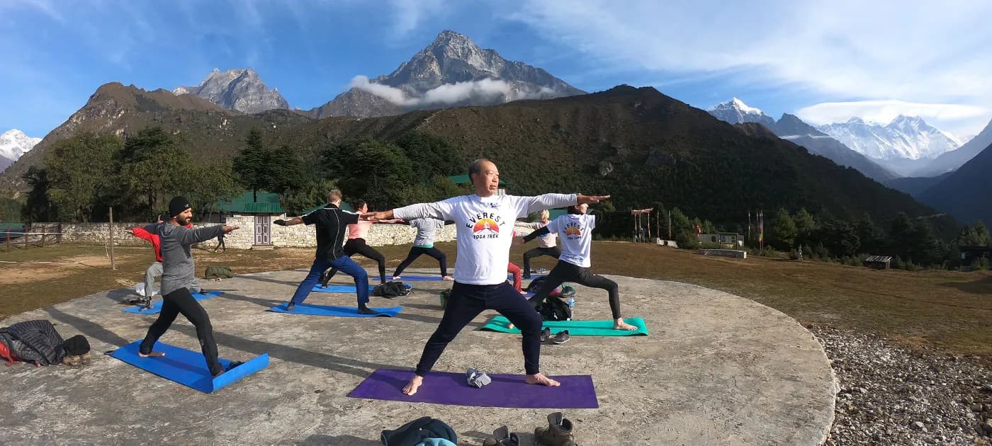 A wide outdoor yoga class held on a circular concrete platform surrounded by Himalayan peaks including Mount Everest and Mount Ama Dablam under a clear blue sky.