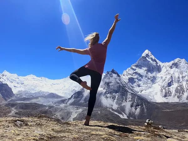 Trekker posing on the Everest Base Camp trail with snow-capped mountain peaks behind her