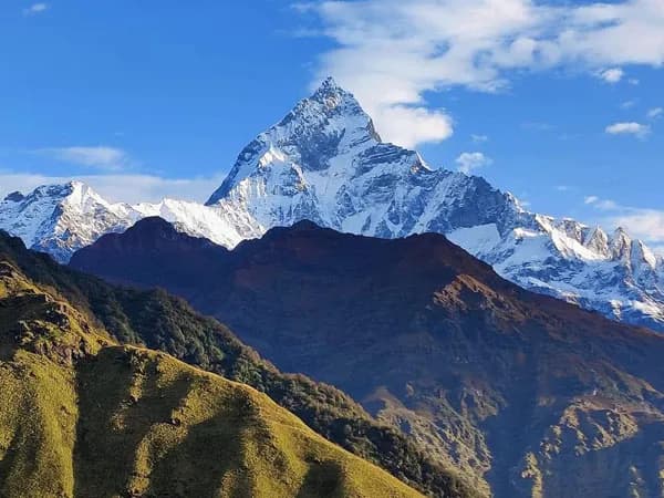 Scenic, close-up view of Mount Machhapuchhre (Fishtail Peak) rising above green mountain ridges under a bright blue sky.