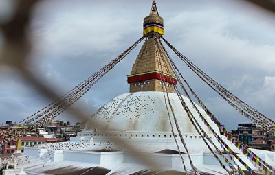 Boudhanath Stupa in Kathmandu Nepal with prayer flags under cloudy sky