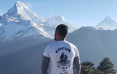 Scenic landscape of Nepal in spring featuring blooming red rhododendrons on green terraced hills with the snow-capped Himalayas in the background.