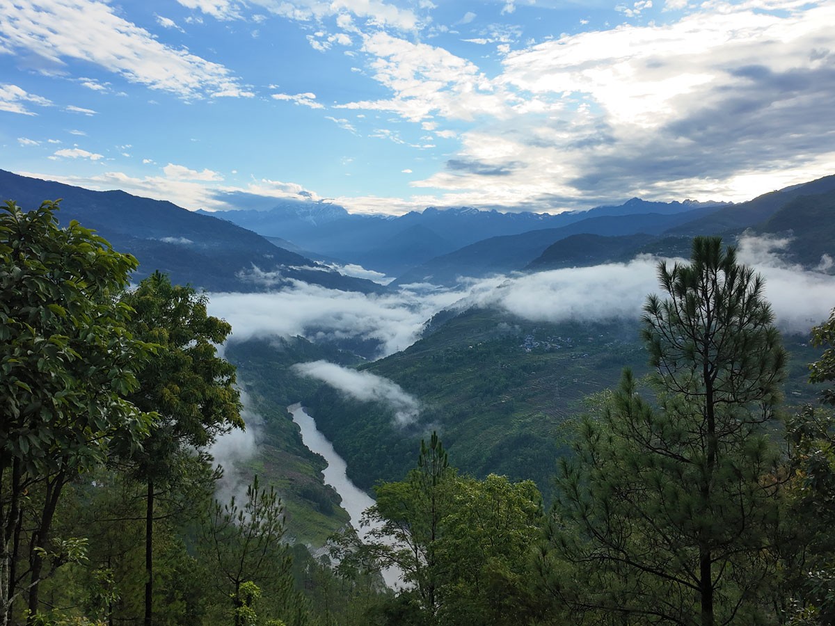 Scenic green mountain valley with river and low clouds in rural Nepal