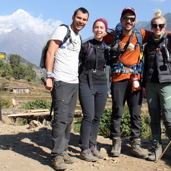 A group of happy hikers pausing near a Chhomrong trail sign on their way to Annapurna Base Camp with Rugged Trails Nepal.