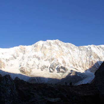 Dramatic silhouetted trekker standing on a rock overlooking the sunlit snow-capped peaks of the Annapurna Sanctuary.
