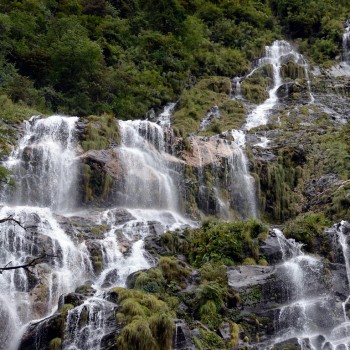 A powerful multi-tiered waterfall cascading down lush green cliffs along the Modi Khola river during the ABC trek.