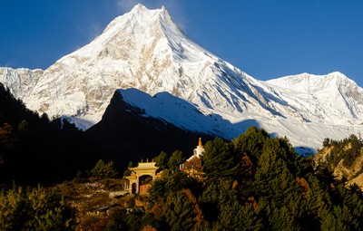 High-altitude view of the snow-capped Mt. Manaslu peak (8,163m) behind a traditional Buddhist stupa and golden-roofed monastery gateway in the Manaslu Conservation Area.